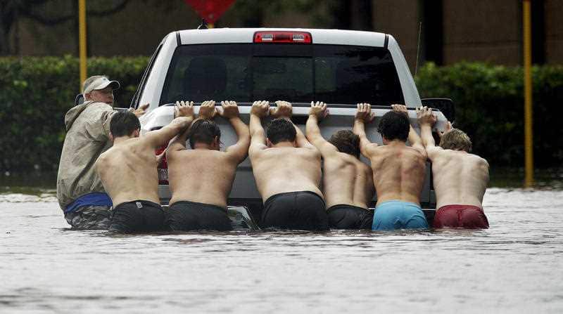 People push a stalled pickup to through a flooded street in Houston, after Tropical Storm Harvey dumped heavy rains Sunday, Aug. 27, 2017. 