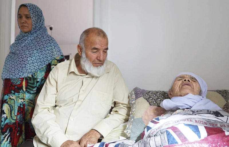 106-year-old Afghan refugee Bibihal Uzbeki rests in bed attended by her son Mohammadollah and daughter-in-law Ziba, in Hova, Sweden.