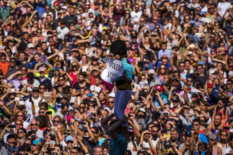 A member of a castelle holds a placard reading in Catalan "We want to vote", as she crowned the human tower in Sant Jaume square in Barcelona, Spain, Sunday, Sept. 24, 2017.