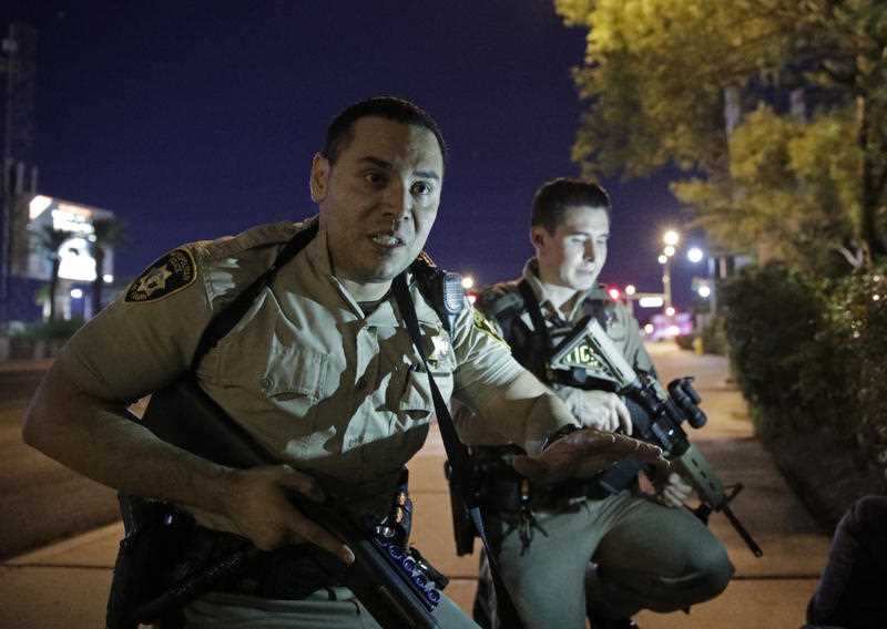 Police officers advise people to take cover near the scene of a shooting near the Mandalay Bay resort and casino on the Las Vegas Strip, Sunday, Oct. 1, 2017, in Las Vegas.