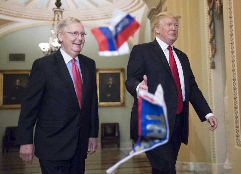 Small Russian flags bearing the word "Trump" are thrown by a protester toward President Donald Trump, as he walks with Senate Majority Leader Mitch McConnell, R-Ky., on Capitol Hill.