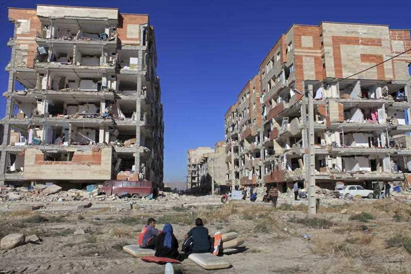 Survivors sit in front of buildings damaged by an earthquake, in Sarpol-e-Zahab, western Iran, Monday, Nov. 13, 2017.
