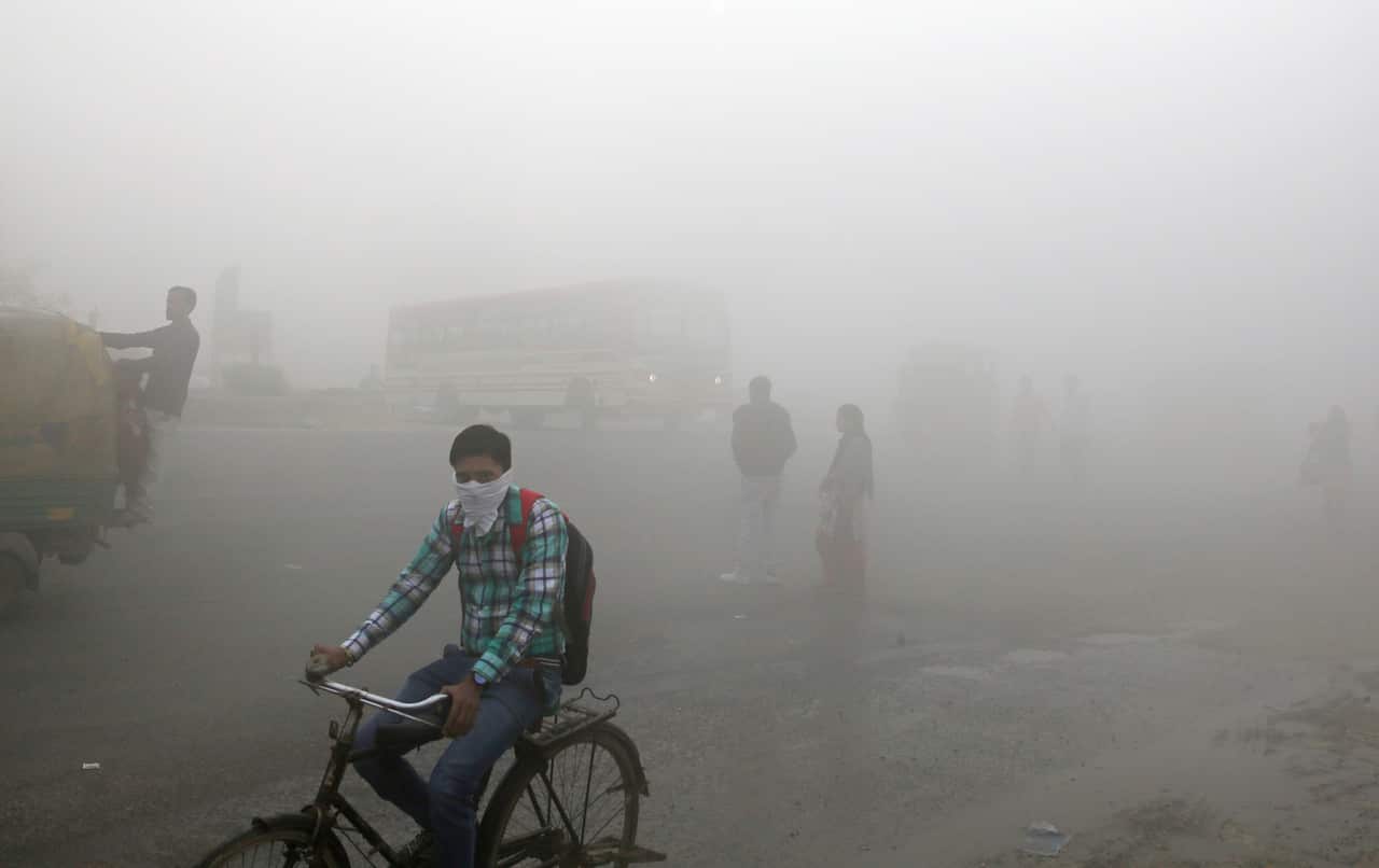 Indian commuters wait for transport amid a thick blanket of smog on the outskirts of New Delhi, India.