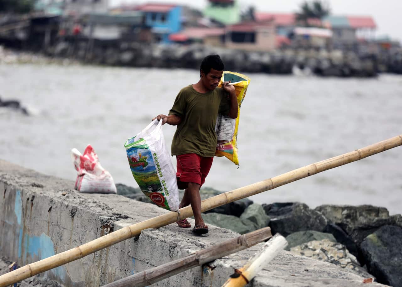 A Filipino resident with his belongings maneuvers on top of a dike at a coastal village in Cavite city.