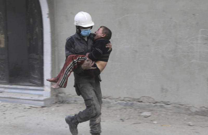 A member of the Syrian Civil Defence group carries a boy who was wounded during airstrikes and shelling by Syrian government forces
