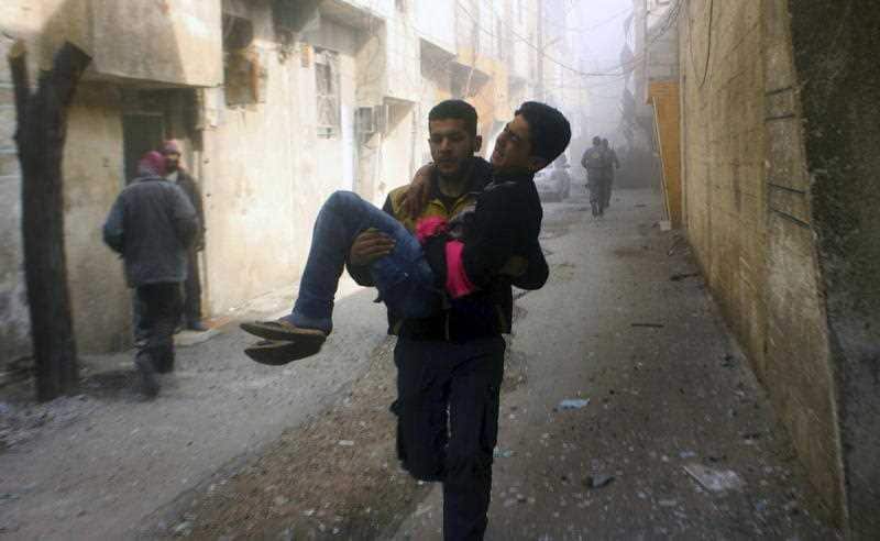 A member of the Syrian Civil Defence group carrying a young man who was wounded during airstrikes and shelling by Syrian government force