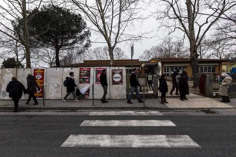 People walk by election posters on March 4, 2018 in San Giuliano Terme near Pisa.