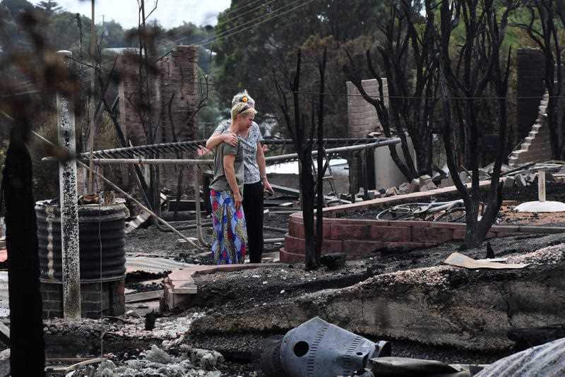 Tathra residents Ingrid Mitchell and Deb Nave wonder through the burnt out remains of their Wildlife Drive home in Tathra.