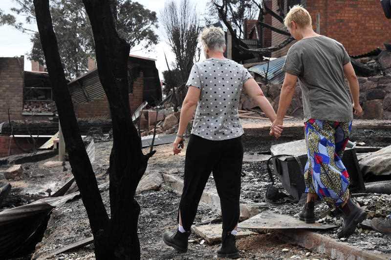 Tathra residents Ingrid Mitchell (right) and Deb Nave (left) wander through the burnt out remains of their Wildlife Drive home in Tathra.