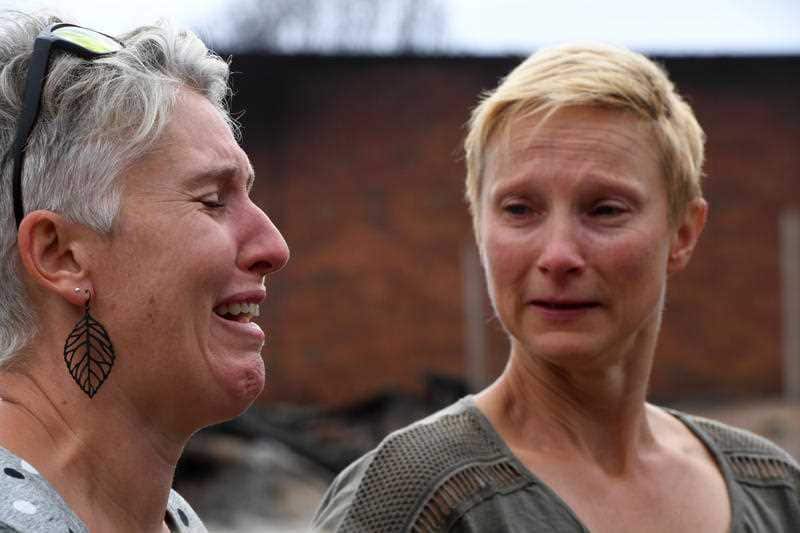 Emotional Tathra residents Ingrid Mitchell (right) and Deb Nave (left) outside the burnt out remains of their Wildlife Drive home in Tathra.