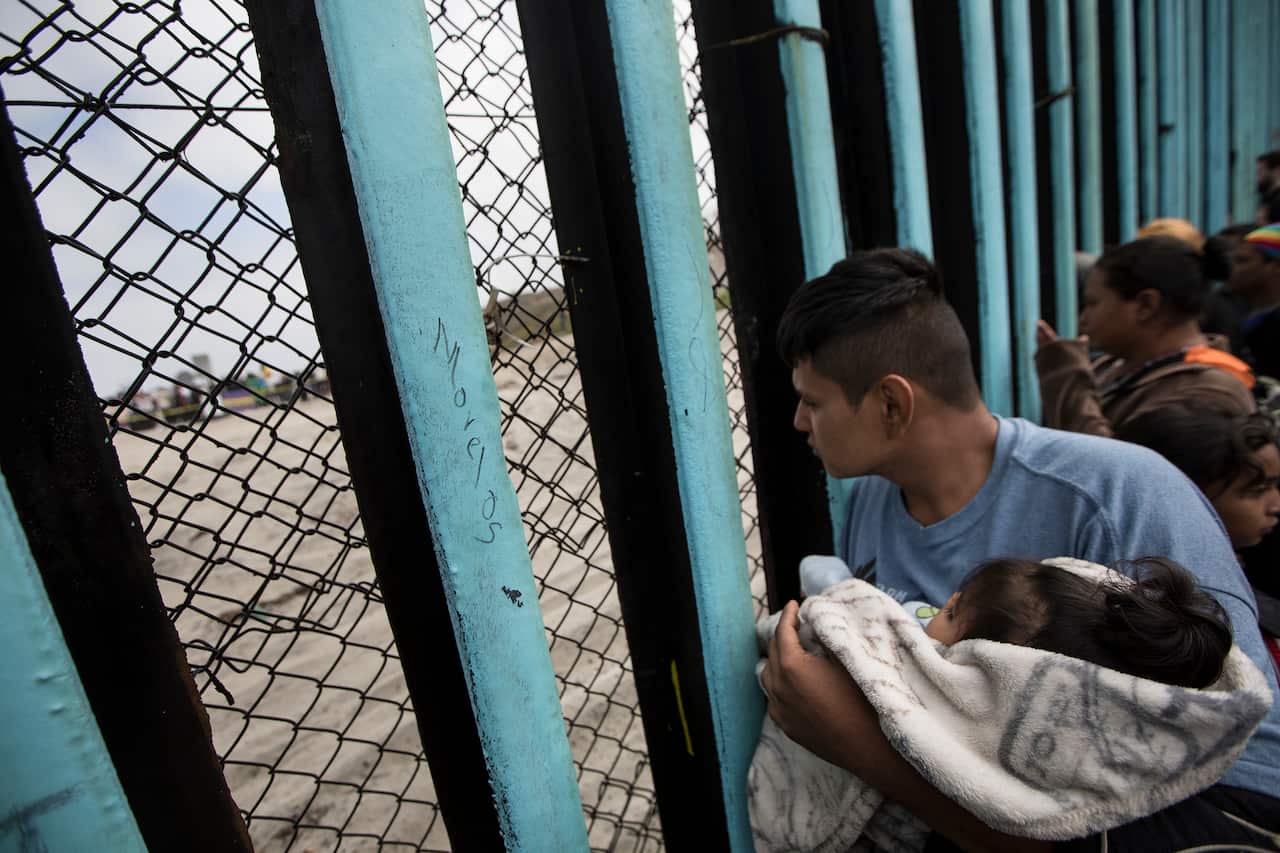 A member of the Central American migrant caravan, holding a child, looks through the border wall toward a group of people gathered on the U side, as he stands on the beach where the border wall ends in the ocean, in Tijuana, Mexico