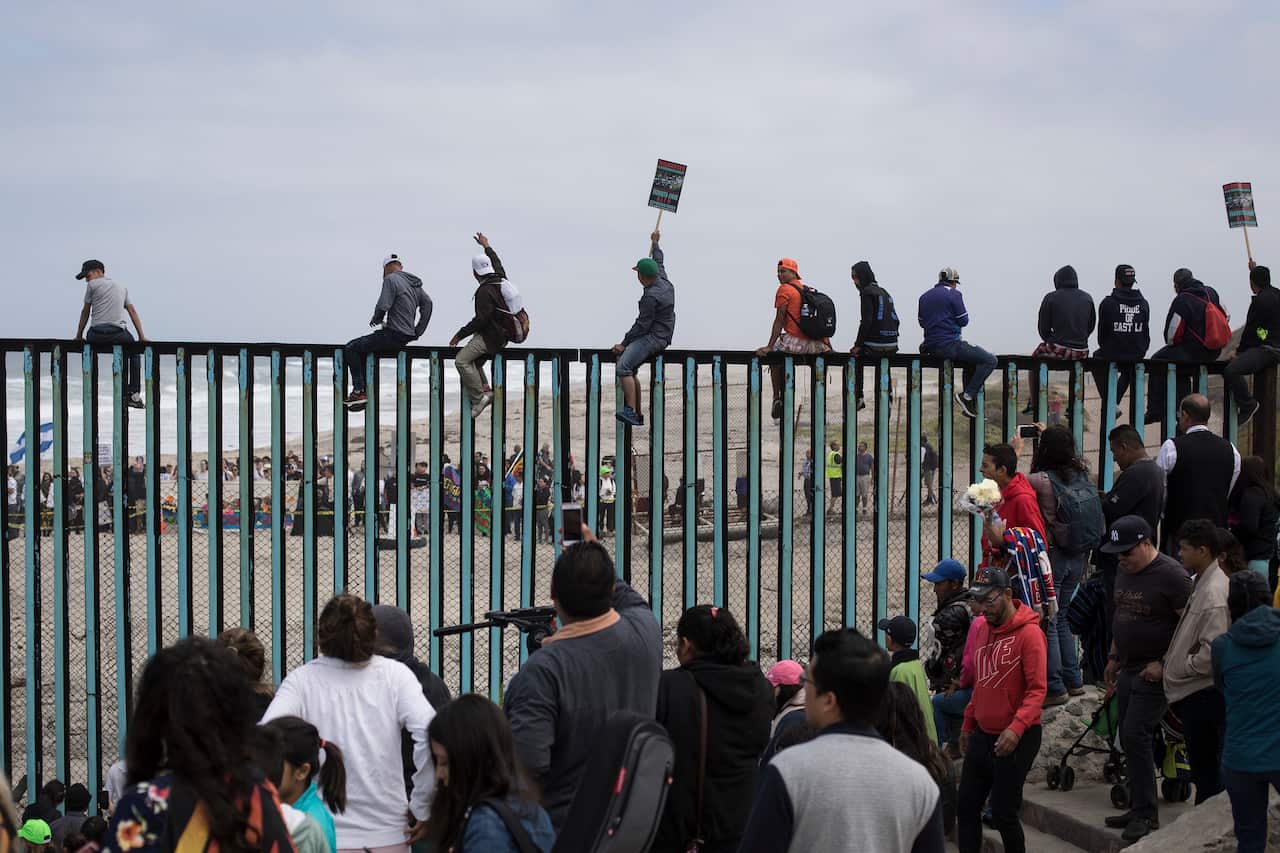 Central American migrants traveling with a caravan gather at the border wall.