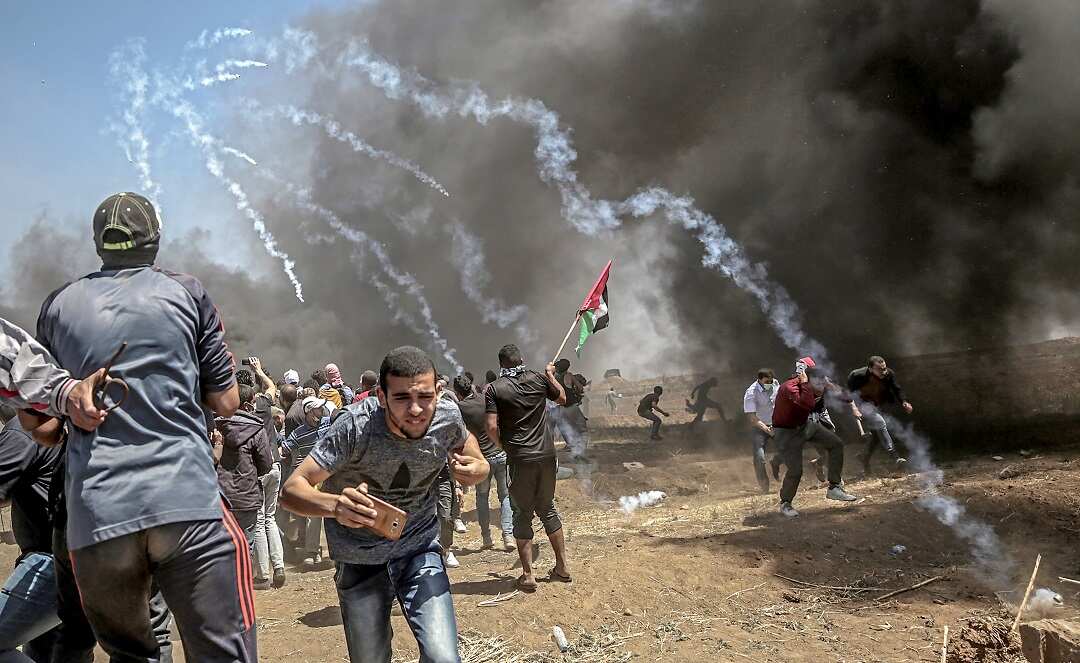 Palestinian protesters run for cover from Israeli tear gas.