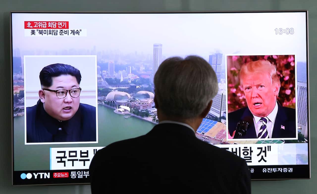 A man watches a TV screen showing file footage of US President Donald Trump, right, and North Korean leader Kim Jong-un
