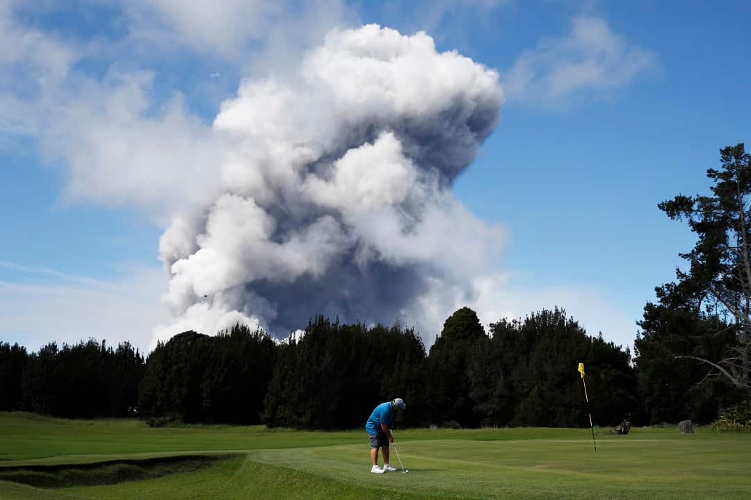 An ash plume rises behind a golf course.