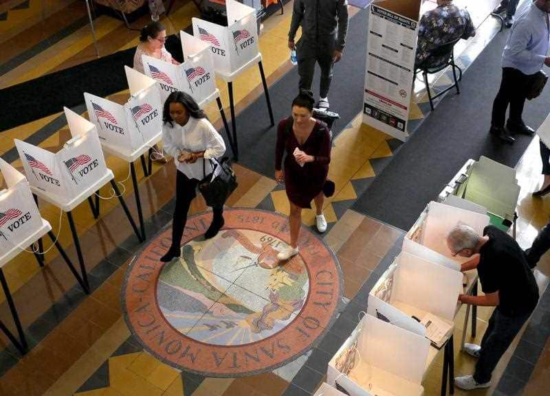 People pass by voters at the Santa Monica City Hall polling station as Californians go to the polls in California's primary election.