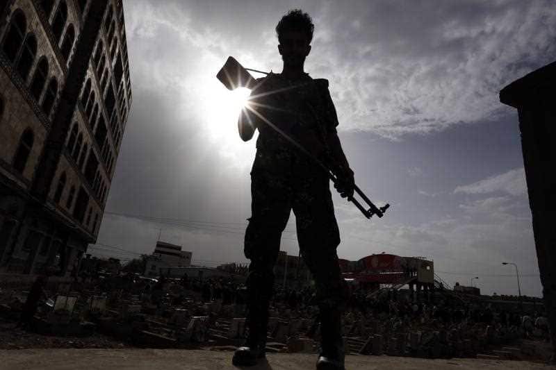 A Yemeni soldier stands guard as people bury the bodies of Houthi militia members allegedly killed during recent fighting at Yemen's western coast areas