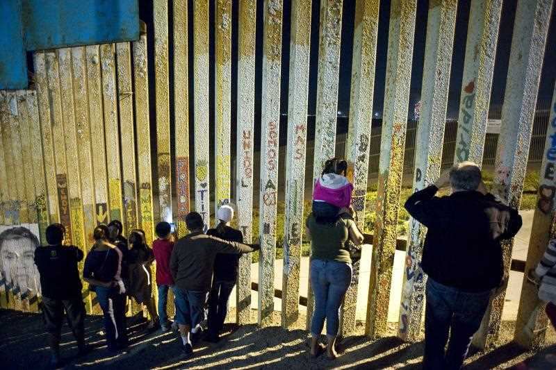 People watch a fireworks display in the United States through the U.S.-Mexico border wall in Tijuana, Mexico, 4 July 2018.