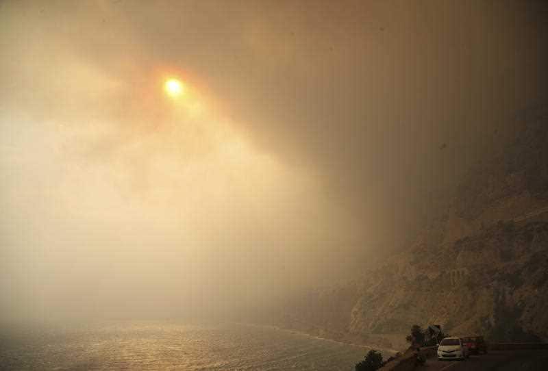 The sun breaks through a smoked filled sky as cars drive on a road near Kineta, west of Athens, Monday, July 23, 2018.