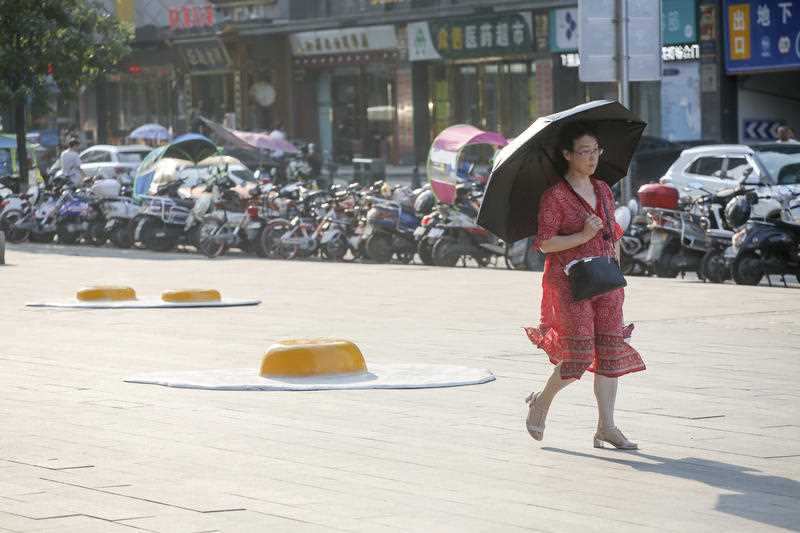 A pedestrian walks past a giant fried egg made of fiber-reinforced plastic installed in front of a shopping mall to illustrate the heat wave in Xi'an city, northwest China's Shaanxi province, 23 July 2018.