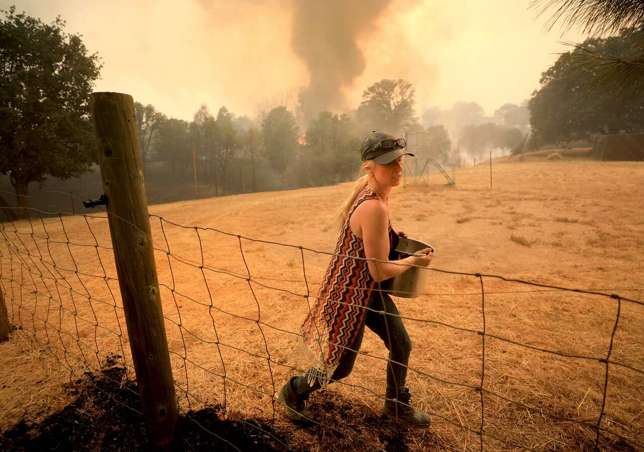 Crystal Easter of Spring Valley uses a pot of water to put spot fires out around her home, as her neighbors home burns to the ground in the background.