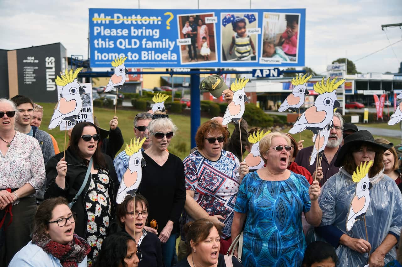 A group of around 100 friends and supporters of the family stand underneath a billboard for the campaign in Brisbane.
