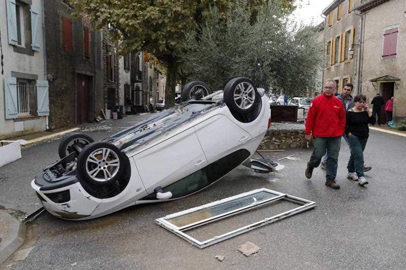 People walk by a damaged car after a storm hit Villegailhenc, France.