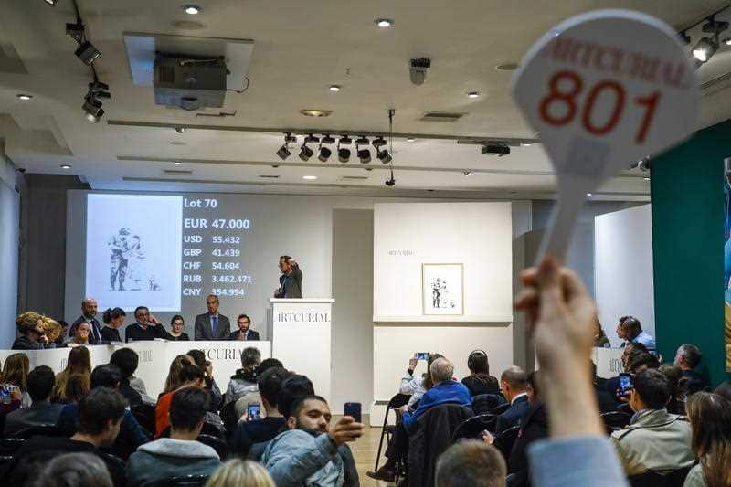 A buyer holds up a paddle to mark a bid during the sale of the offset lithograph 'Stop and Search' (2007) by British artist Banksy.