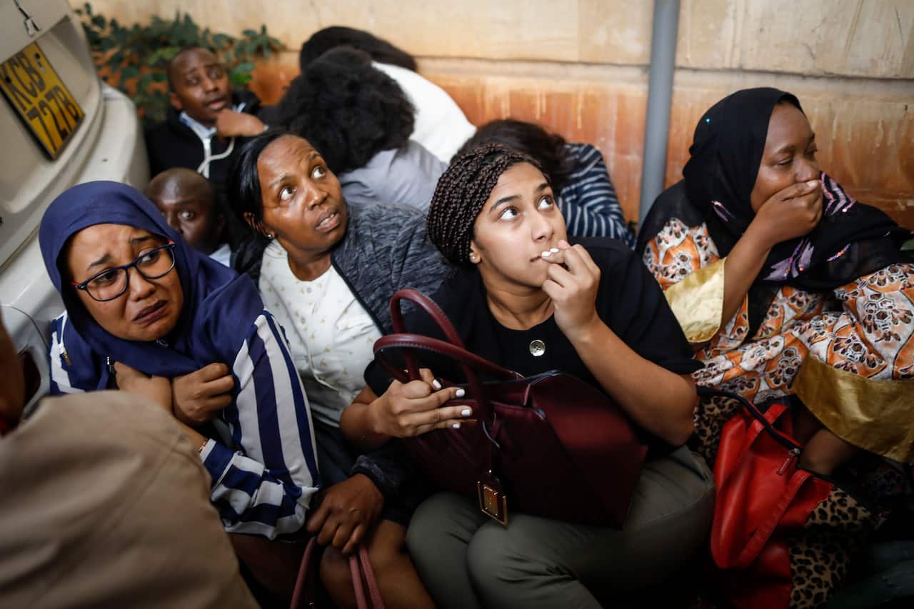 Women wait to be escorted after evacuating out of the building window, during an ongoing gunfire and explosions in Nairobi.