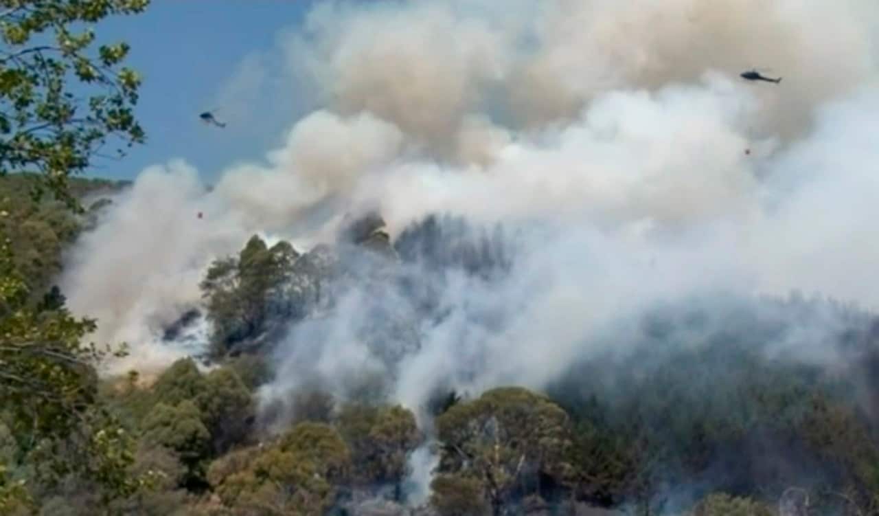 Helicopters drop water on a wildfire coming over a ridge near a residential area, Friday, Feb. 8, 2019, in Wakefield, New Zealand.