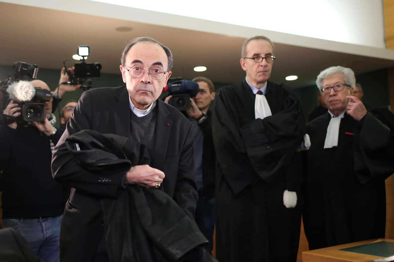Cardinal Philippe Barbarin, center, takes his seat as he arrives at the Lyon courthouse with his lawyers in Lyon, central France. 