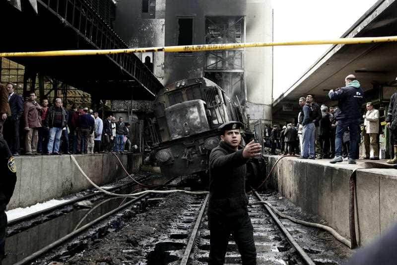 Policemen stand guard in front of a damaged train.