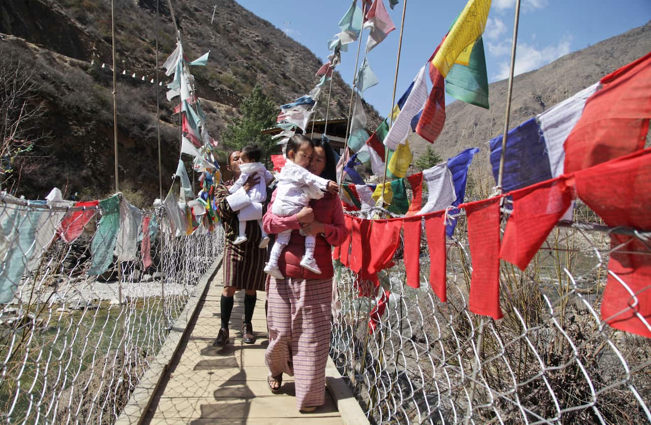 Twin sisters Nima and Dawa are carried across a bridge by their mother Bhumchu Zangmo and father Sonam Tshering.