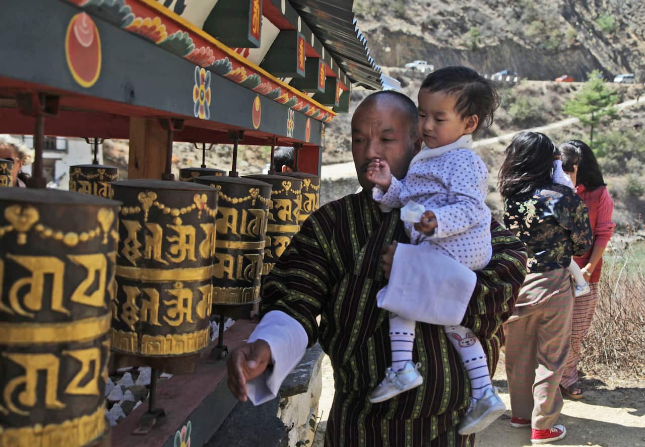 Sonam Tshering holds one of his conjoined twin daughters and spins prayer wheels at the Tachog Lhakhang Buddhist temple.
