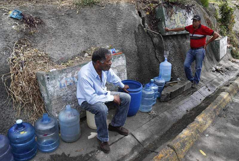 Men fill containers with water at Avila National Park during rolling blackouts 