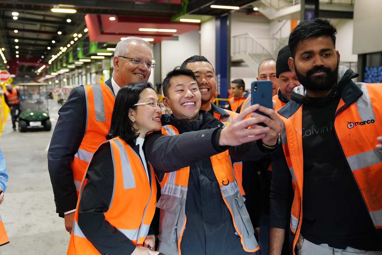 Prime Minister Scott Morrison and Liberal candidate for Chisholm Gladys Liu pose for a selfie with workers during a visit to the Melbourne Markets in Melbourne, Thursday, March 14, 2018. (AAP Image/Stefan Postles) NO ARCHIVING