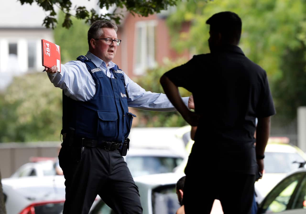 A police officer attempts to move people away from across the road from a mosque in central Christchurch, New Zealand, Friday.