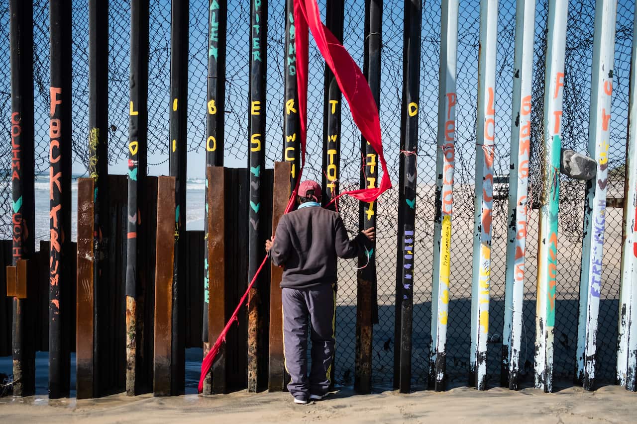 A young boy is seen peaking through the fence at the Mexico-US border before slipping through the fence.