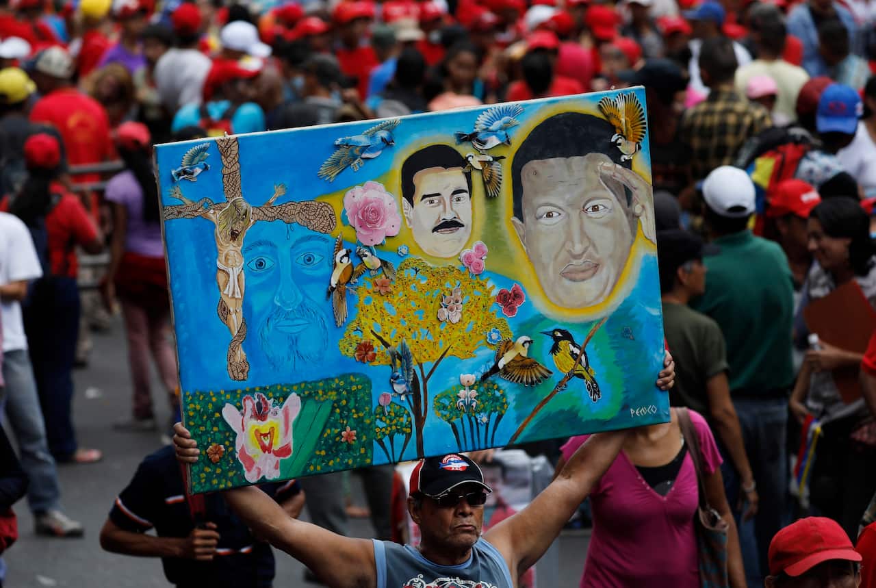 A supporter of President Nicolas Maduro holds a painting depicting the late president Hugo Chavez on the right corner, and President Nicolas Maduro.