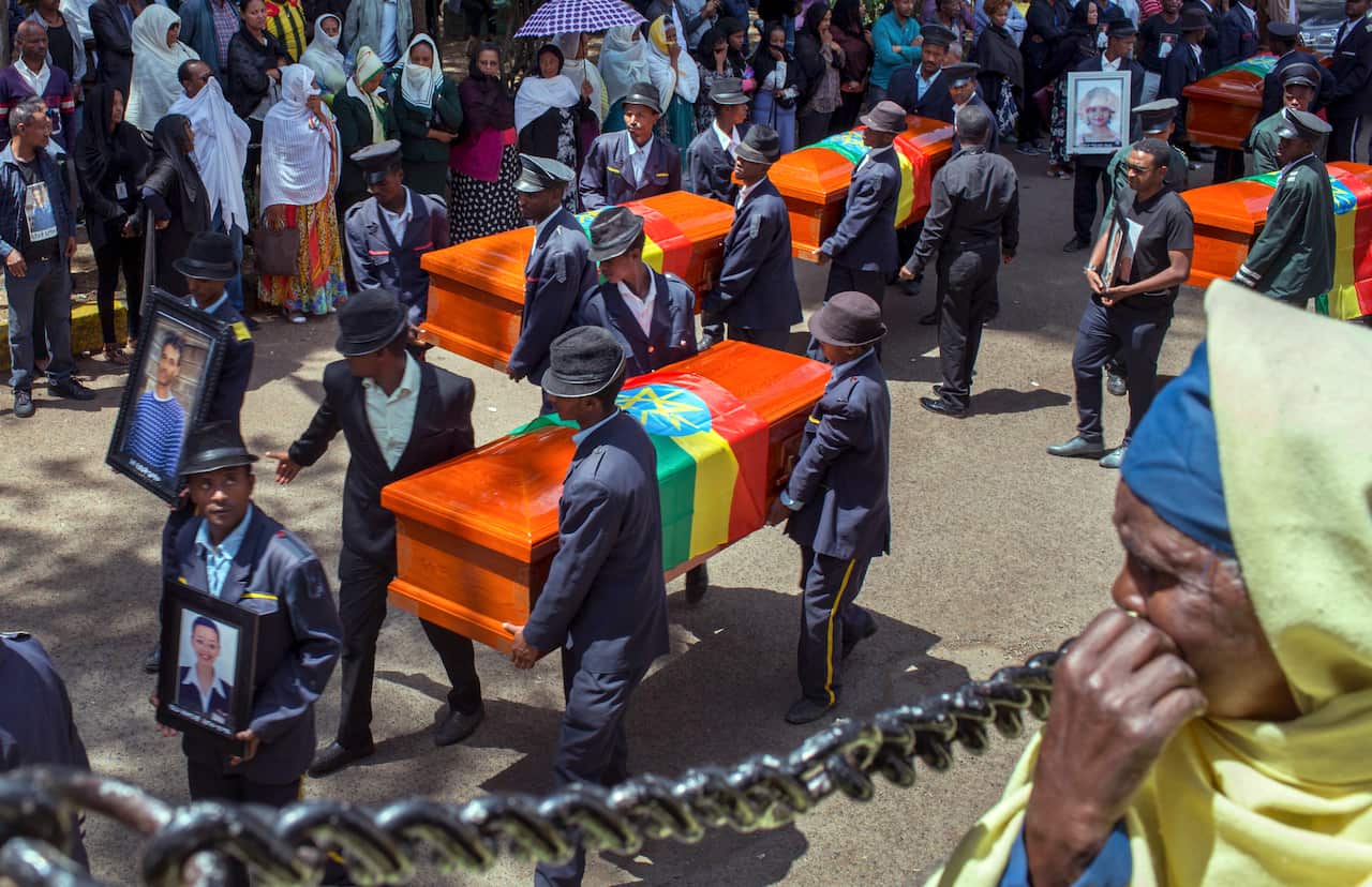 Relatives grieve next to empty caskets draped with the national flag.