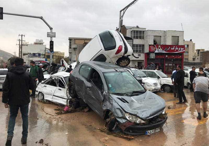People stand near destroyed cars after a flood hit the city of Shiraz, Iran