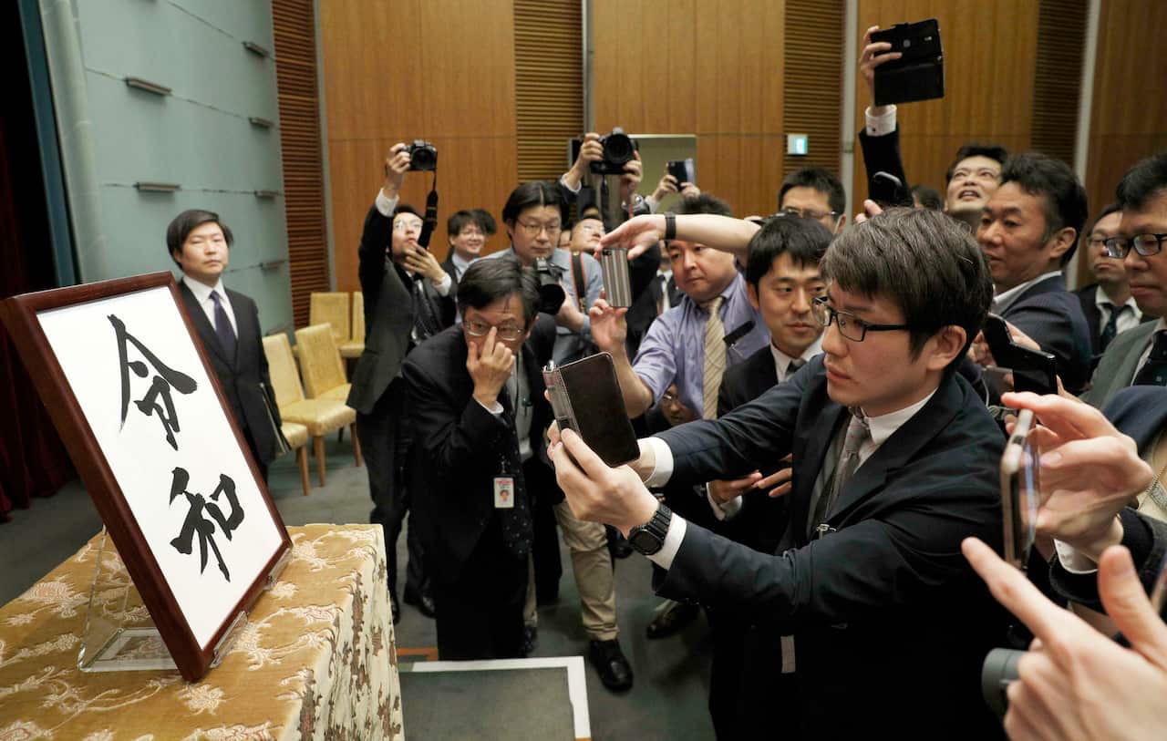 Media gathers in front of a piece of calligraphy showing the name of Japan's new era Reiwa.