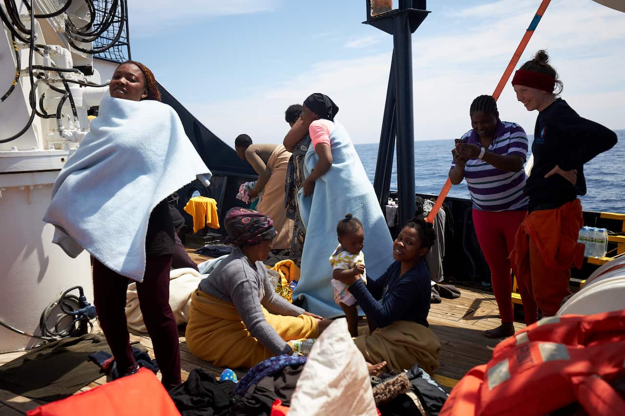 Migrants stand on the dock of the Sea-Watch rescue ship