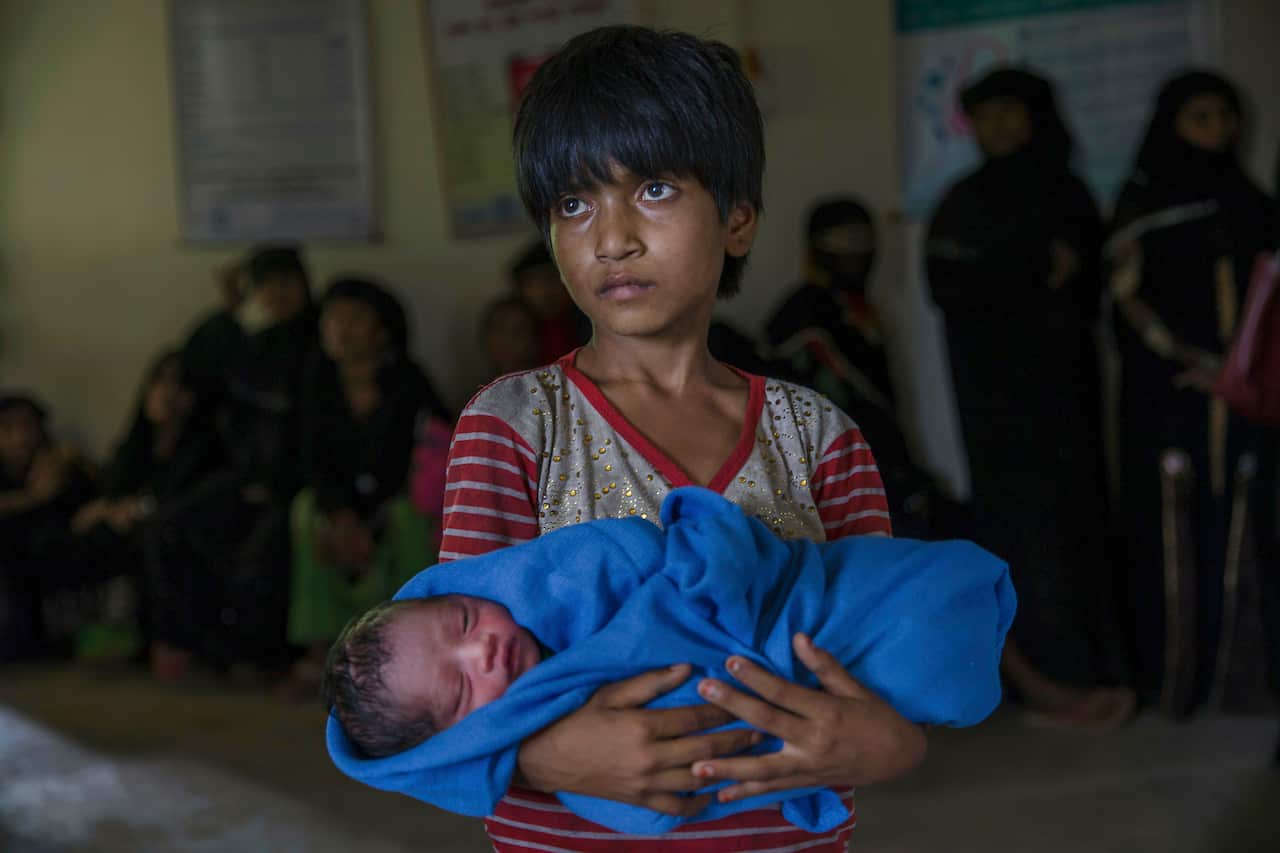 Rohingya Muslim girl Afeefa Bebi, holds her brother as doctors check her mother Yasmeen Ara at a community hospital in Kutupalong refugee camp, Bangladesh 2017.