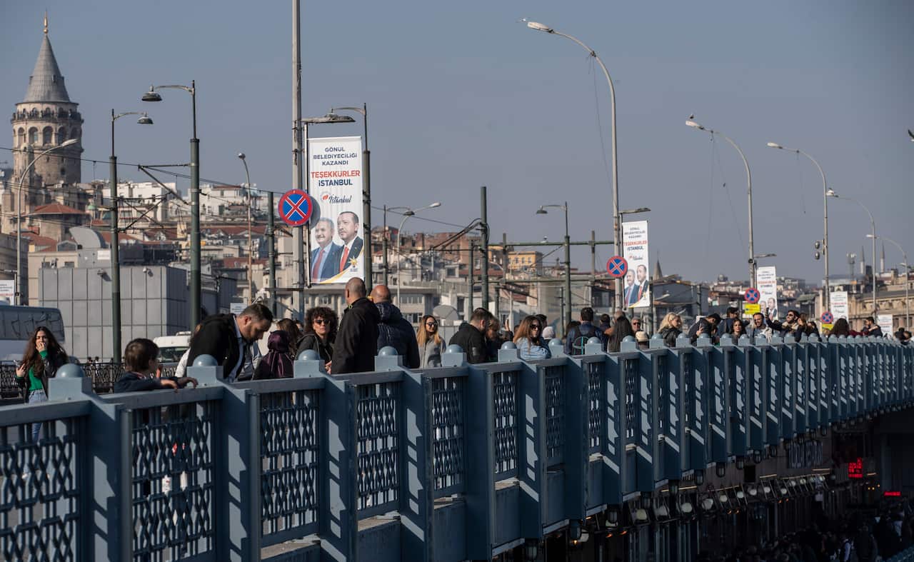 People walk on Galata Bridge as they pass in front of a picture of Turkish President Recep Tayyip Erdogan, in Istanbul, Turkey.
