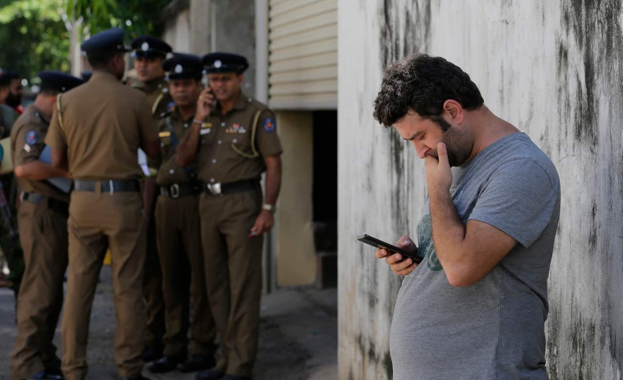 A foreigner checks his mobile phone while waiting outside a mortuary of a hospital, a day after series of blasts, in Colombo, Sri Lanka.