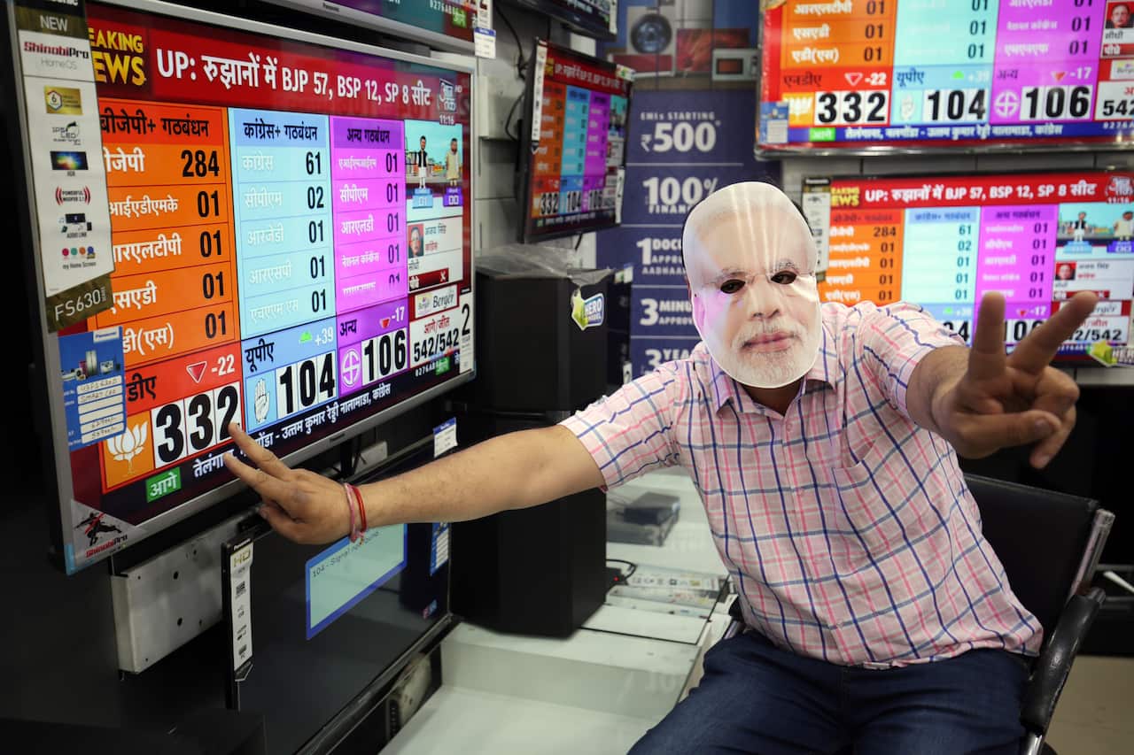 A BJP supporter wearing a mask depicting Indian Prime Minister Narendra Modi flashes victory signs.