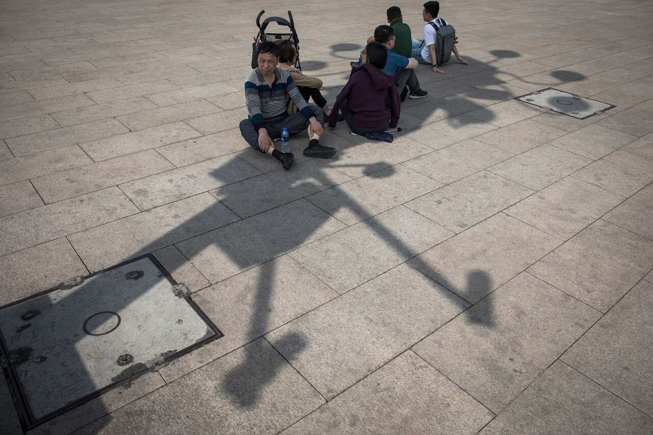 Chinese tourists rest beneath the shadow of a lamp post holding surveillance cameras on the Tiananmen Square.
