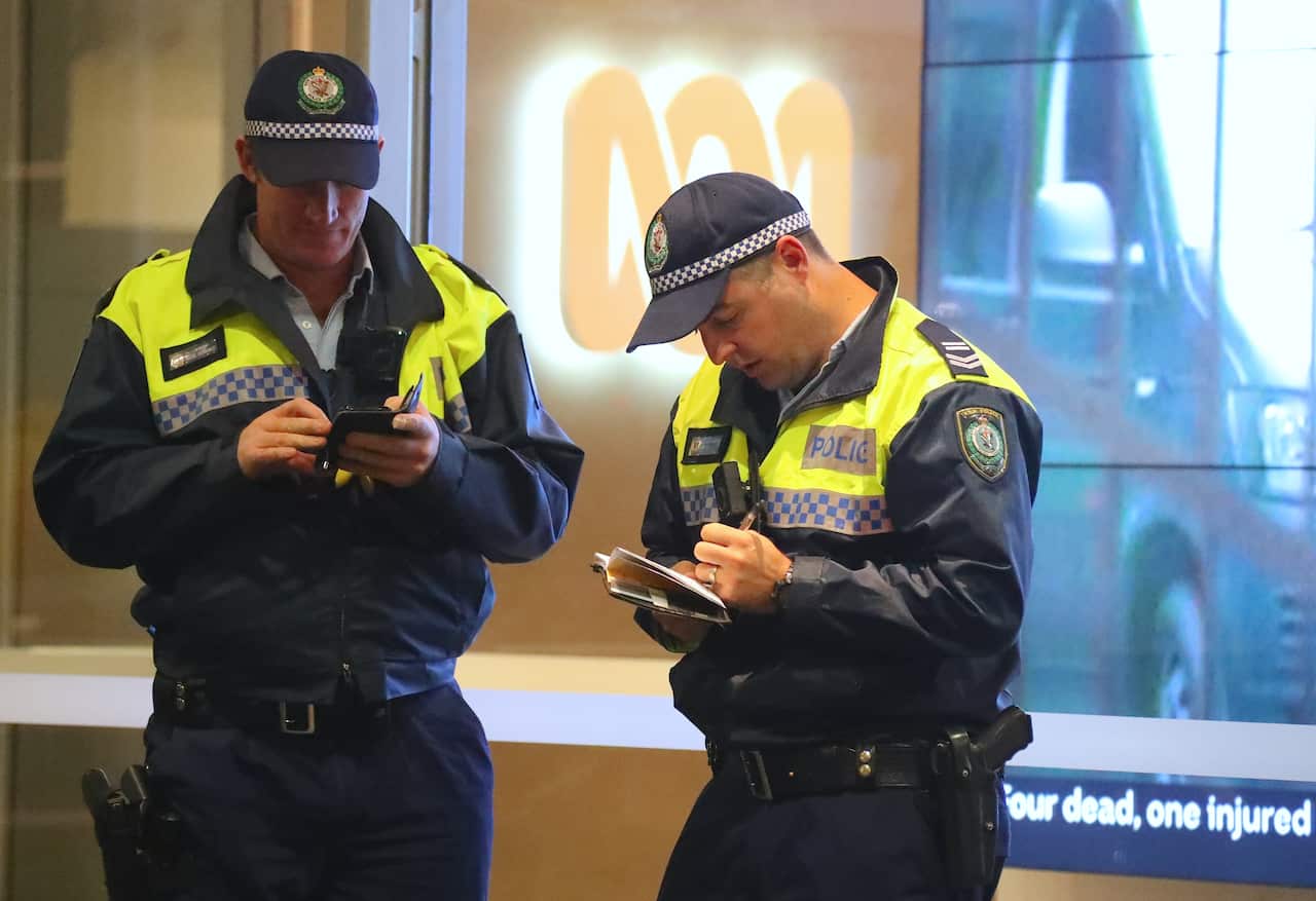 Two policemen stand in front of an ABC logo at the main entrance to the ABC in Sydney.