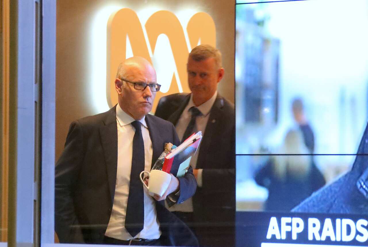 John Lyons (left), Executive Editor of ABC News, is followed by an Australian Federal Police officer as they walk out the main entrance to the ABC building